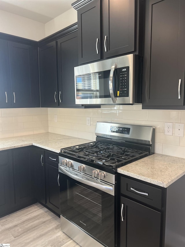 kitchen with backsplash, stainless steel appliances, light stone countertops, and light wood-type flooring