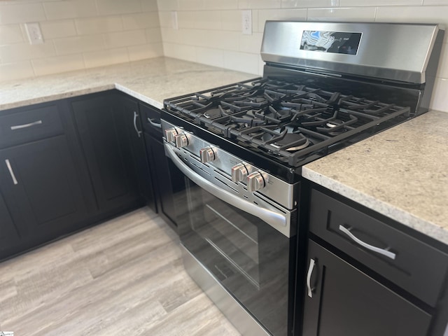 kitchen with light stone counters, light wood-type flooring, decorative backsplash, and stainless steel gas range oven