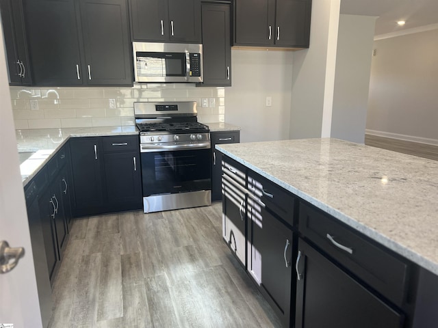 kitchen with appliances with stainless steel finishes, decorative backsplash, light stone counters, and light hardwood / wood-style flooring