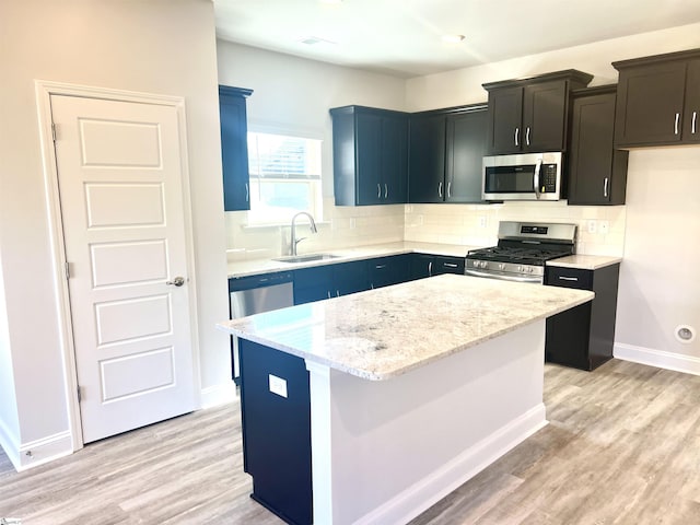 kitchen with appliances with stainless steel finishes, sink, decorative backsplash, a center island, and light hardwood / wood-style floors