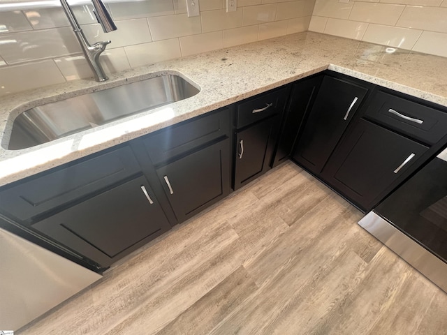 kitchen with sink, decorative backsplash, light stone countertops, and light wood-type flooring