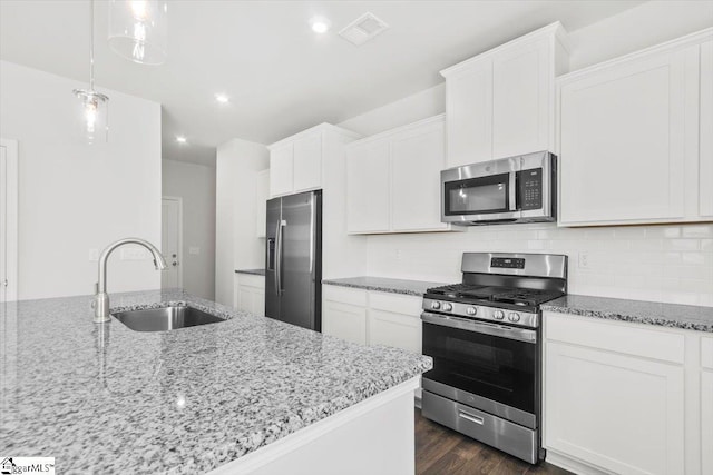 kitchen with stainless steel appliances, light stone counters, a sink, and white cabinetry