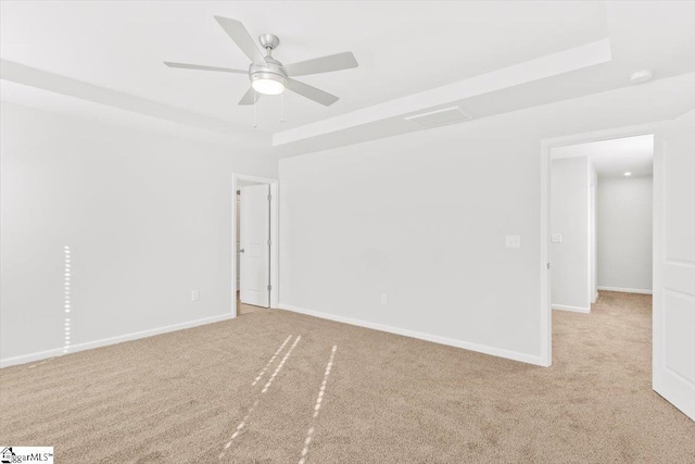 empty room featuring a tray ceiling, light carpet, ceiling fan, and baseboards