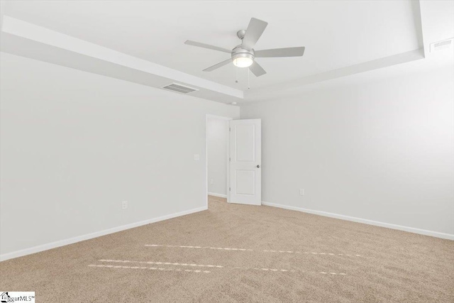 carpeted empty room featuring baseboards, visible vents, a tray ceiling, and a ceiling fan