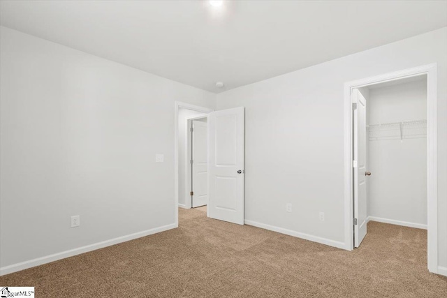 unfurnished bedroom featuring light carpet, a spacious closet, and baseboards