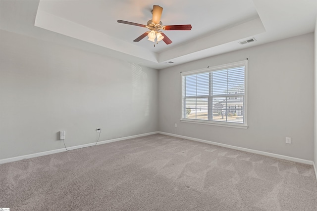 empty room with light colored carpet, ceiling fan, and a tray ceiling