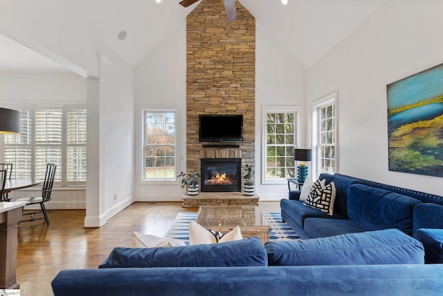 living room featuring ceiling fan, high vaulted ceiling, a fireplace, and light hardwood / wood-style floors