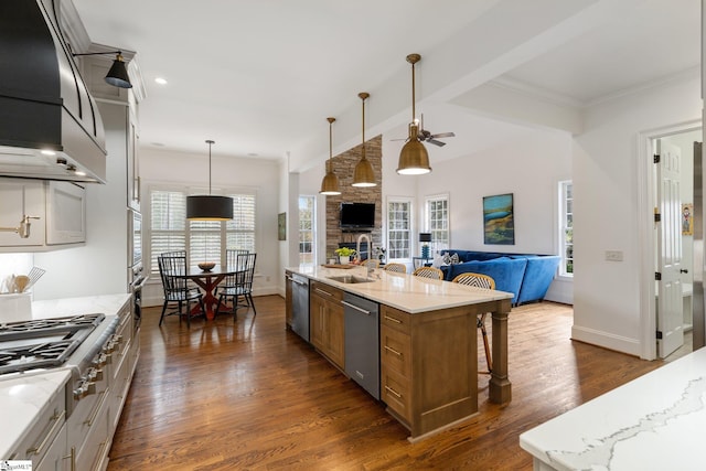 kitchen featuring a large island with sink, light stone countertops, pendant lighting, and stainless steel appliances