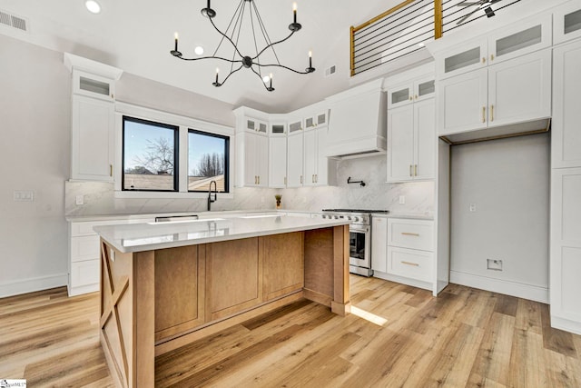 kitchen with stainless steel range, white cabinets, custom range hood, a kitchen island, and backsplash