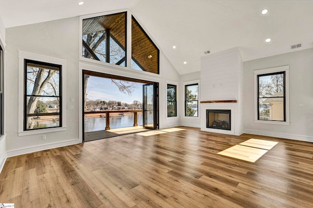 unfurnished living room with high vaulted ceiling, a large fireplace, a water view, and light wood-type flooring