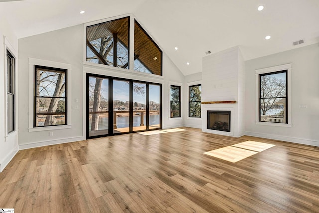 unfurnished living room with light hardwood / wood-style flooring, high vaulted ceiling, and a large fireplace