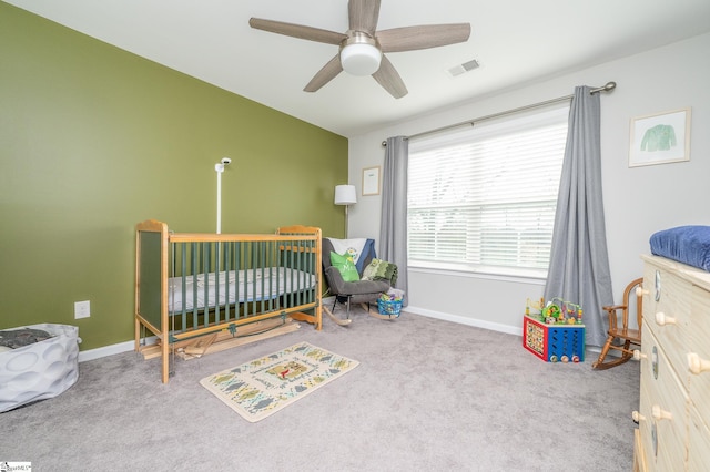 bedroom featuring ceiling fan, light colored carpet, and a crib