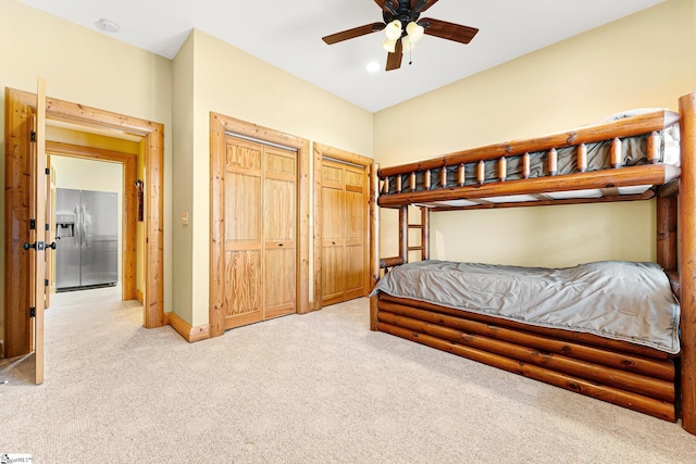 carpeted bedroom featuring stainless steel fridge with ice dispenser, multiple closets, and ceiling fan