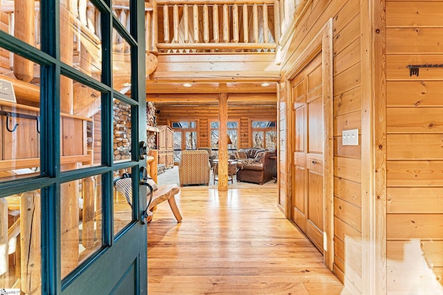 corridor featuring a high ceiling, log walls, wooden walls, and light hardwood / wood-style flooring