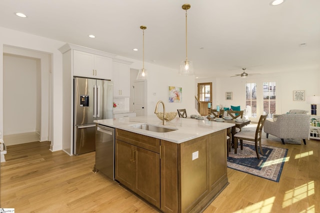 kitchen featuring sink, light wood-type flooring, an island with sink, stainless steel appliances, and white cabinets