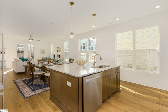 kitchen with sink, light hardwood / wood-style flooring, stainless steel dishwasher, an island with sink, and pendant lighting