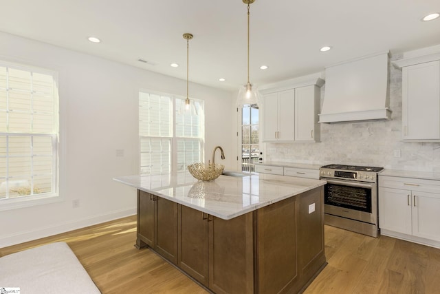 kitchen featuring custom exhaust hood, an island with sink, white cabinets, and stainless steel gas stove