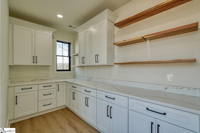 kitchen with white cabinetry, light stone countertops, and light wood-type flooring