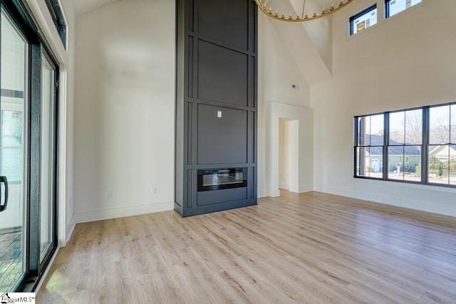 unfurnished living room with a towering ceiling, light hardwood / wood-style flooring, and a notable chandelier