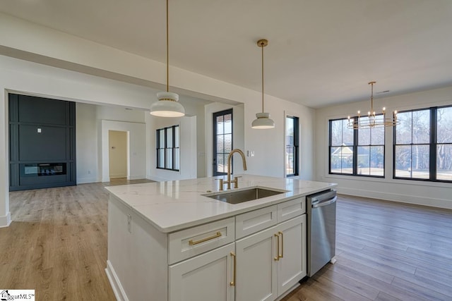 kitchen with white cabinetry, sink, stainless steel dishwasher, light stone counters, and a center island with sink