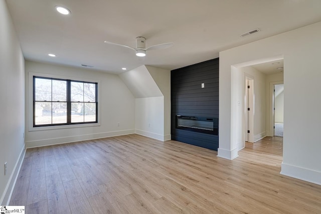 additional living space featuring a fireplace, ceiling fan, and light hardwood / wood-style flooring