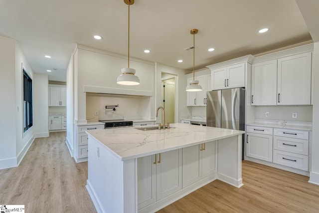 kitchen with sink, hanging light fixtures, stainless steel refrigerator, light stone countertops, and white cabinets