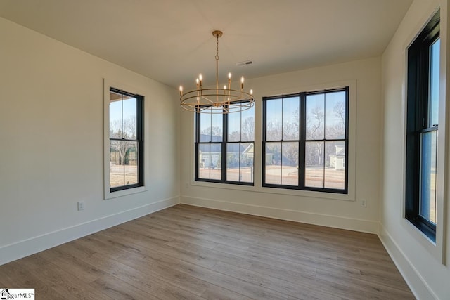 unfurnished dining area featuring an inviting chandelier and wood-type flooring