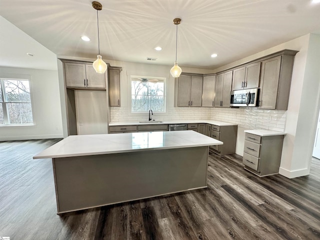 kitchen with stainless steel appliances, light stone countertops, a center island, and decorative light fixtures