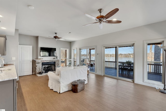 living room featuring ceiling fan, a stone fireplace, and light hardwood / wood-style flooring