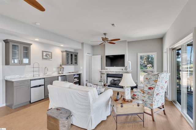 living room featuring a fireplace, sink, wine cooler, ceiling fan, and light hardwood / wood-style floors