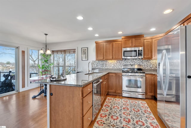 kitchen featuring sink, decorative light fixtures, light wood-type flooring, dark stone countertops, and appliances with stainless steel finishes