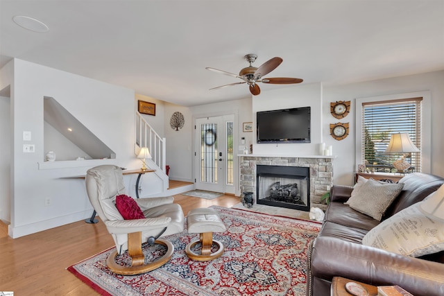 living room with a stone fireplace, ceiling fan, and light hardwood / wood-style flooring