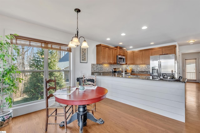 kitchen with tasteful backsplash, light wood-type flooring, kitchen peninsula, pendant lighting, and stainless steel appliances