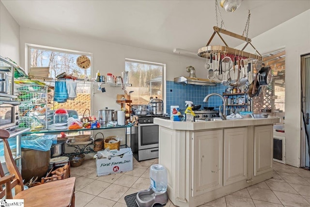 kitchen with light tile patterned flooring, stainless steel range with gas cooktop, a center island with sink, and backsplash