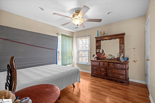 bedroom with ceiling fan, wood-type flooring, and a textured ceiling