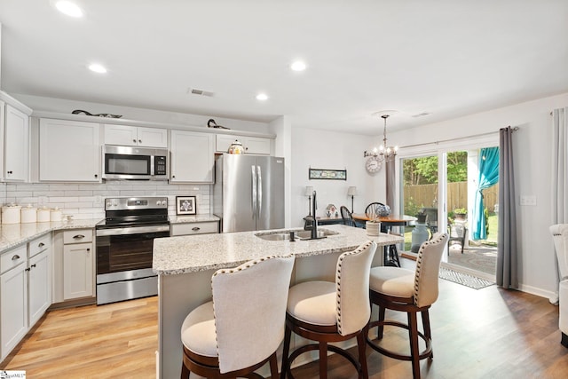 kitchen with an island with sink, sink, white cabinets, hanging light fixtures, and stainless steel appliances