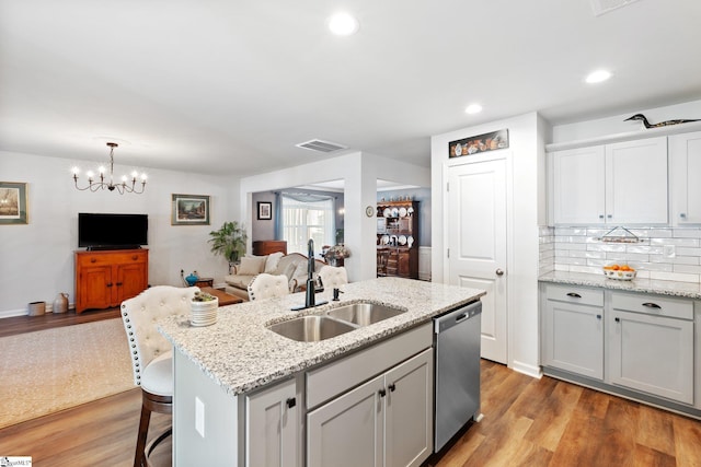 kitchen with sink, light hardwood / wood-style floors, a center island with sink, decorative light fixtures, and stainless steel dishwasher