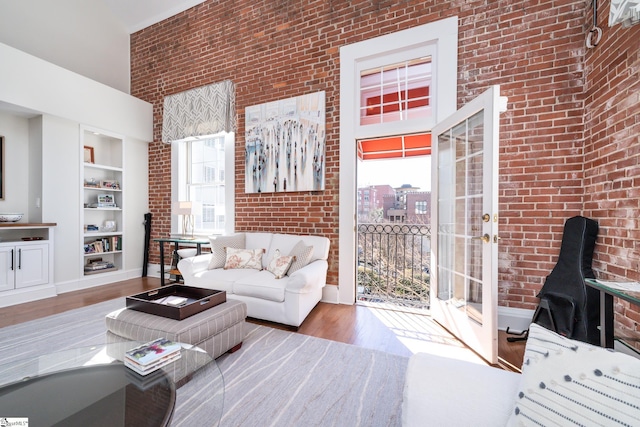 living room with hardwood / wood-style flooring, brick wall, a high ceiling, and built in shelves