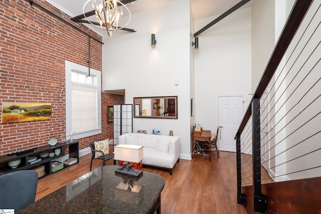 living room featuring brick wall, a towering ceiling, dark wood-type flooring, and a notable chandelier