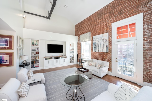 living room with a high ceiling, brick wall, plenty of natural light, and hardwood / wood-style floors