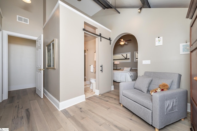 sitting room with a barn door, high vaulted ceiling, beam ceiling, and light wood-type flooring