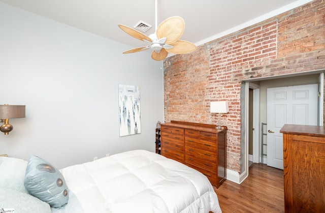 bedroom with ceiling fan, brick wall, and wood-type flooring