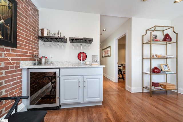 bar with beverage cooler, light stone countertops, hardwood / wood-style floors, and white cabinets