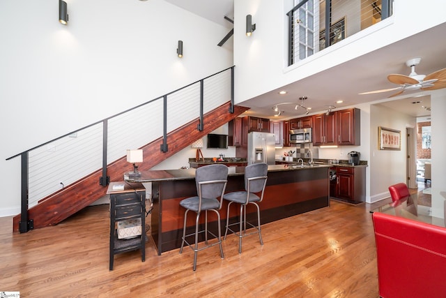 kitchen with a kitchen bar, ceiling fan, stainless steel appliances, light hardwood / wood-style floors, and a high ceiling