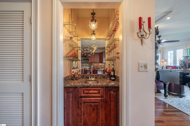 bar with sink, ceiling fan, dark stone countertops, dark hardwood / wood-style floors, and decorative light fixtures