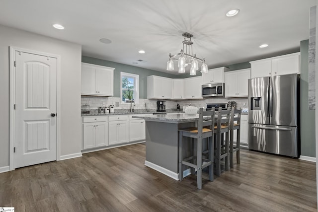 kitchen with light stone counters, decorative light fixtures, a center island, appliances with stainless steel finishes, and white cabinets