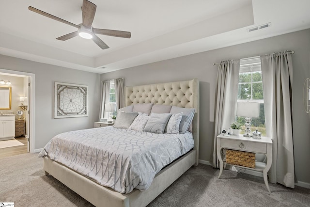 bedroom with a tray ceiling, ensuite bath, ceiling fan, and carpet