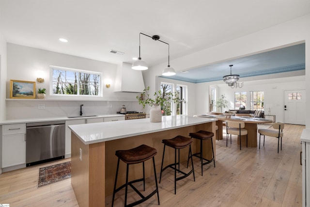 kitchen featuring a kitchen island, white cabinetry, sink, stainless steel dishwasher, and wall chimney range hood