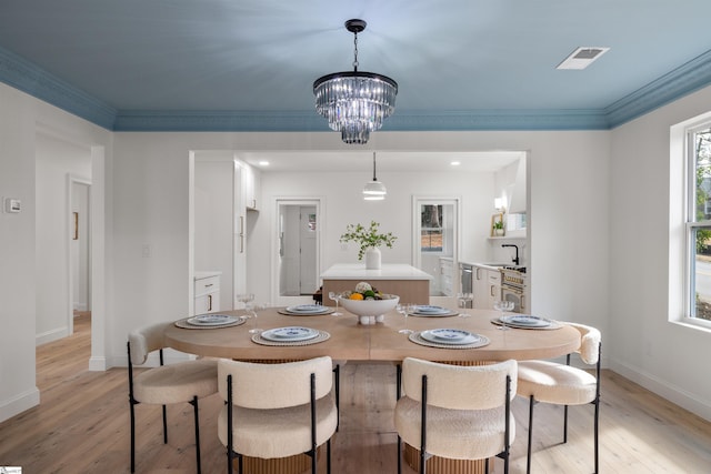 dining area with crown molding, sink, an inviting chandelier, and light hardwood / wood-style floors