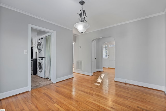 unfurnished dining area with crown molding, stacked washer / drying machine, and light hardwood / wood-style flooring